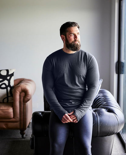 Man wearing a casual work out shirt sitting on a gray armchair in a room with a couch and decorative pillows.