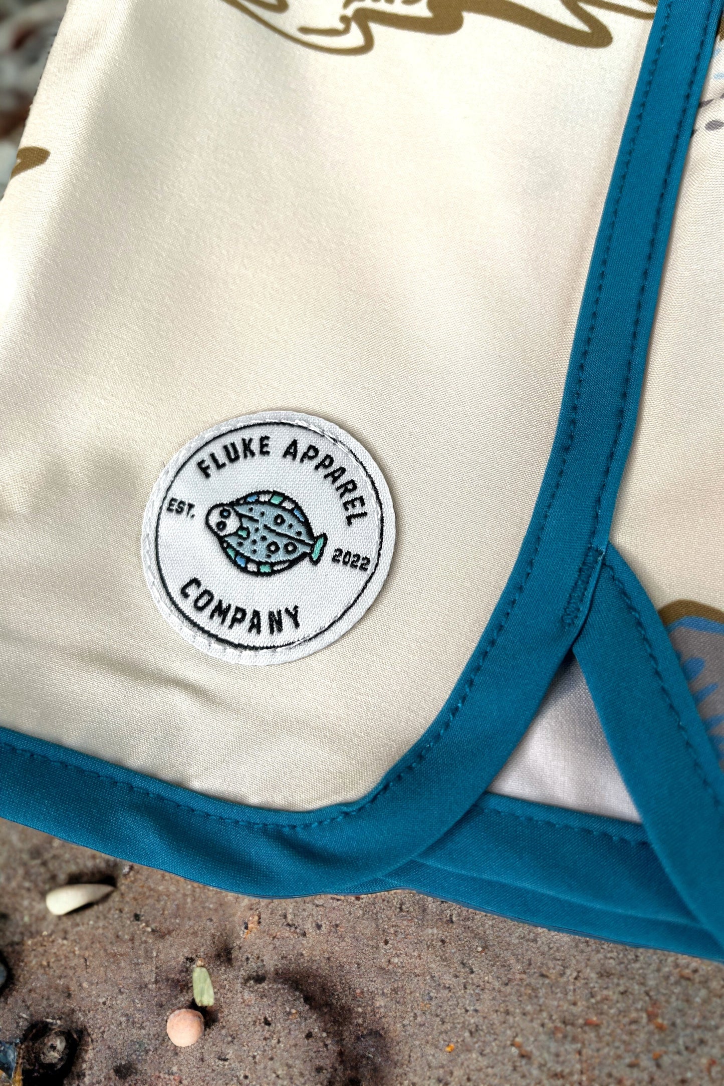 Beige fabric with blue trim and Fluke Apparel Company logo on a sandy background